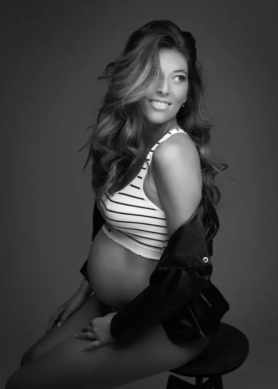 Portrait d'une femme souriante enceinte assise sur un tabouret. elle porte une brassière à rayure