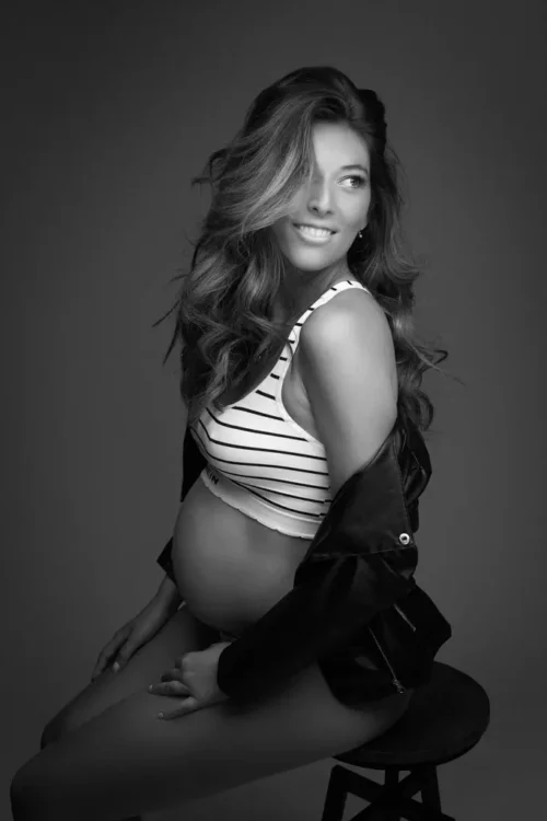 Portrait d'une femme souriante enceinte assise sur un tabouret. elle porte une brassière à rayure