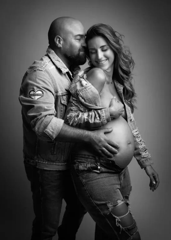 photo en noir et blanc d'un couple avec une femme enceinte. Habillés en jean ils sont souriant.