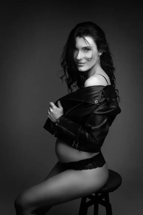 Portait d'une femme enceinte assise sur un tabouret portant un perfecto, les cheveux dans le vent