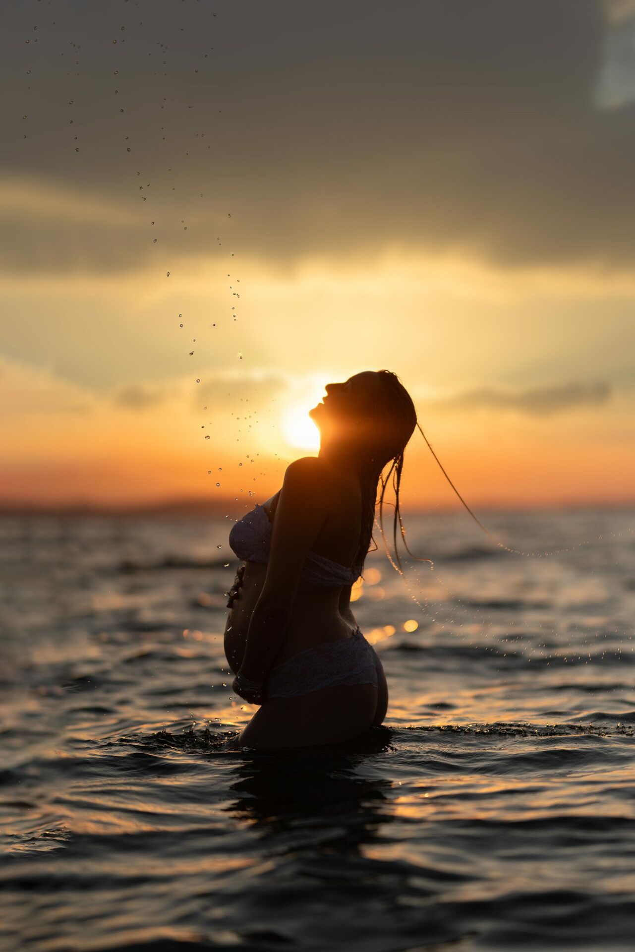 femme enceinte en maillot dans l'eau avec coucher de soleil sur une plage dans les bouches du rhone
